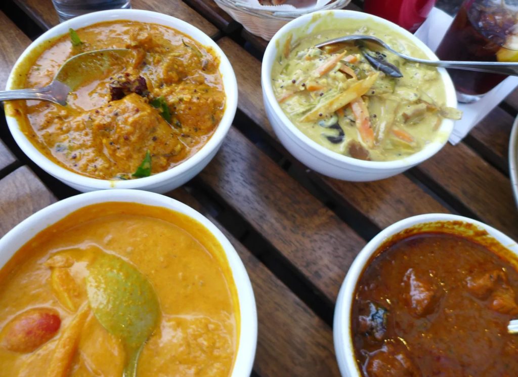 Four-bowls-of-curry-in-shades-of-brown-dark-red-and-orange-on-a-slatted-table